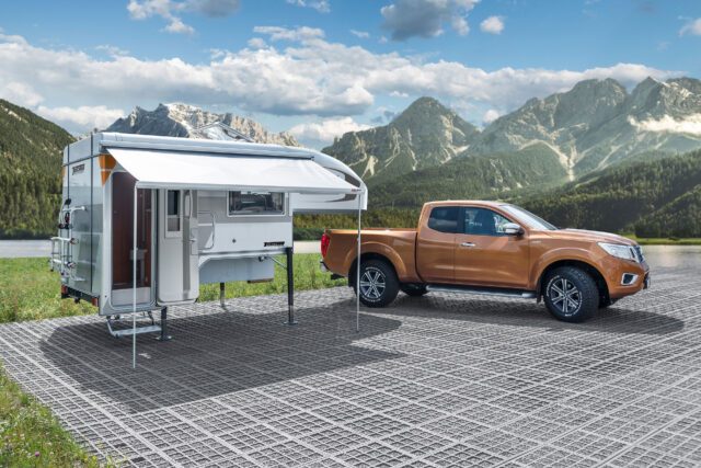 Tischer-Kabine freistehend auf Abstellfläche mit goldfarbenem Pickup daneben, Berge im Hintergrund.