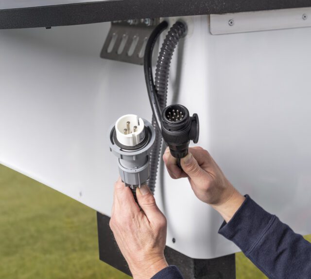 Stromanschluss an Tischer Kabine – Hand verbindet externe Stromzufuhr.