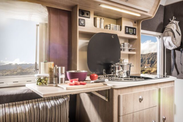 Moderne Küchenzeile mit Spüle, Gaskocher und Regalen – warme Lichtstimmung und wohnliches Ambiente.