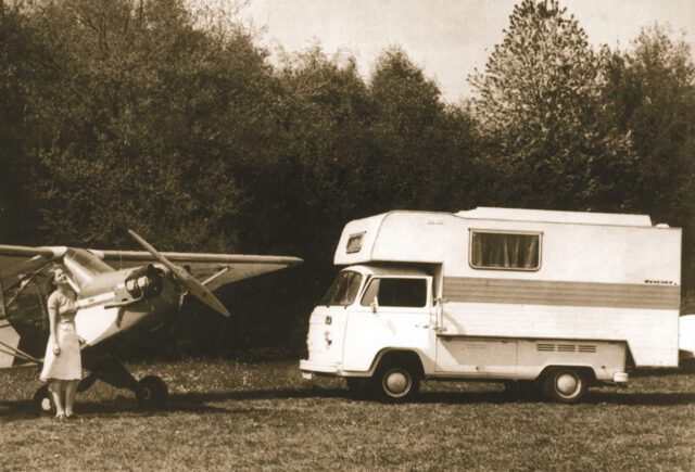 1978_Schwarz-weiß-Aufnahme: Tischer-Kabine auf Transporter mit Propellerflugzeug im Hintergrund.