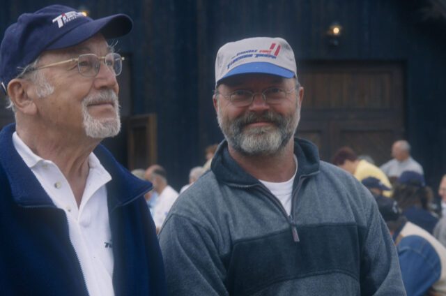 1990_Zwei Männer mit Tischer-Basecap – Nahaufnahme mit lächelndem Blick in die Kamera.