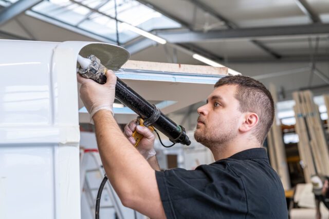 Tischer Wohnkabinen Fertigung - Mitarbeiter trägt Dichtmasse mit Kartuschenpistole auf Außenteil auf.