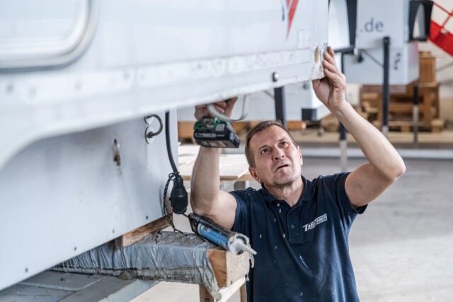 Tischer Absetzkabinen Manufaktur - Techniker arbeitet an Kabinenunterboden – Blick von unten auf Mechanik.