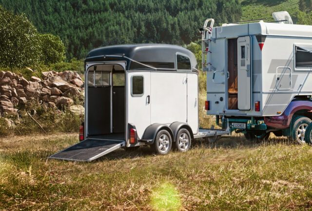 Pferde-Anhänger mit geöffneter Rampe neben einem Pick-up mit Tischer-Wohnkabine in der Natur