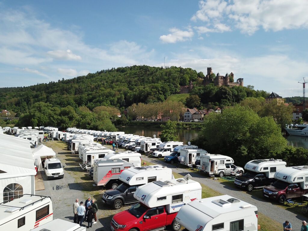 Stellplatz mit vielen Tischer-Wohnkabinen aufgereiht am Mainufer, im Hintergrund die Ruine der Burg Wertheim.