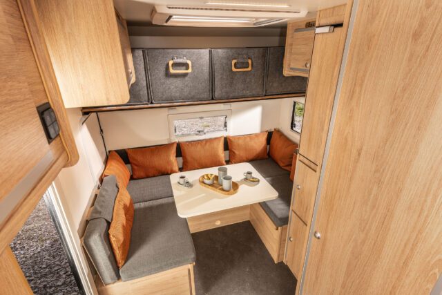 Sitzgruppe in der Tischer Trail 260SP, umgebaut zum Bett mit oranger Bettwäsche und Kissen.