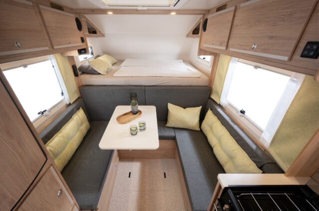 Innenraum mit Sitzgruppe und hochgeklapptem Doppelbett in Fahrtrichtung, Fenster auf beiden Seiten.