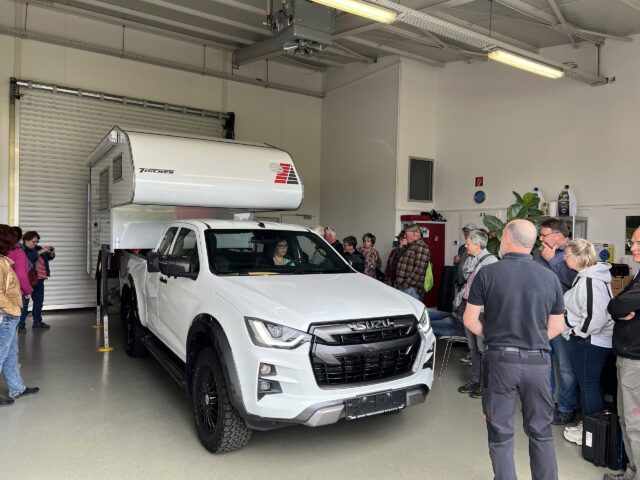 Ankunft einer Tischer-Kabine in einer Werkstatthalle – mehrere Personen stehen neugierig um das Fahrzeug.