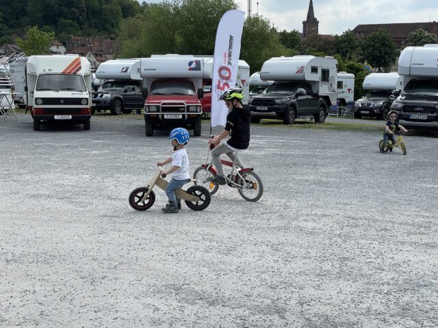 Zwei Kinder fahren auf Laufrad und Fahrrad über den Platz des Tischer-Treffens – im Hintergrund viele Kabinen.
