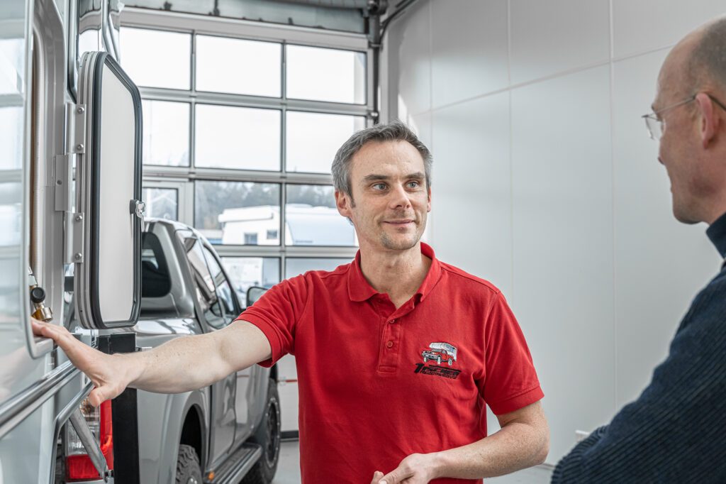 Mitarbeiter von Tischer in rotem Poloshirt beim Kundengespräch in der Ausstellungshalle – Blick zur Seite.