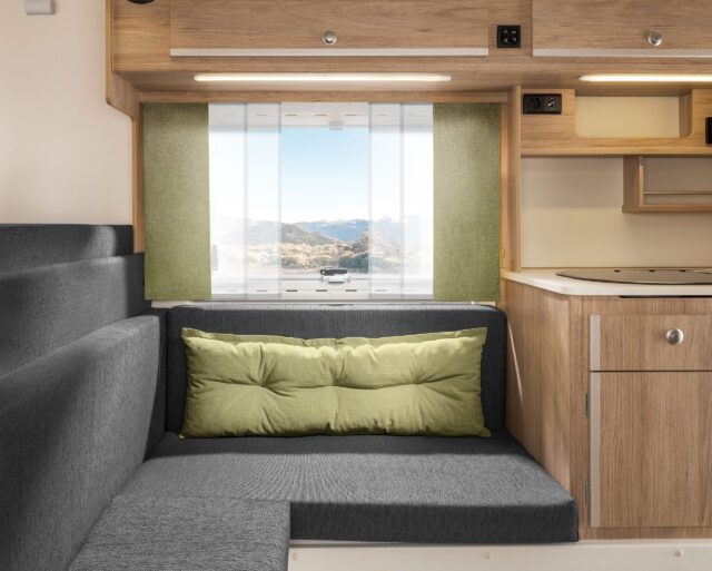 Tischer Sitzgruppe mit grauen Polstern und grünen Vorhängen.