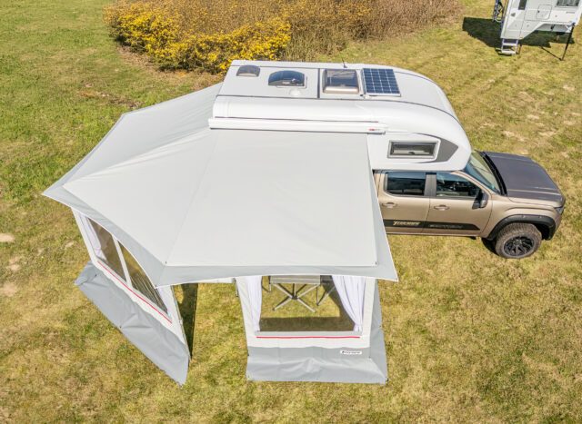 Freistehendes Vorzelt mit weißen Seitenwänden neben Tischer-Wohnkabine – Luftaufnahme auf Wiese.