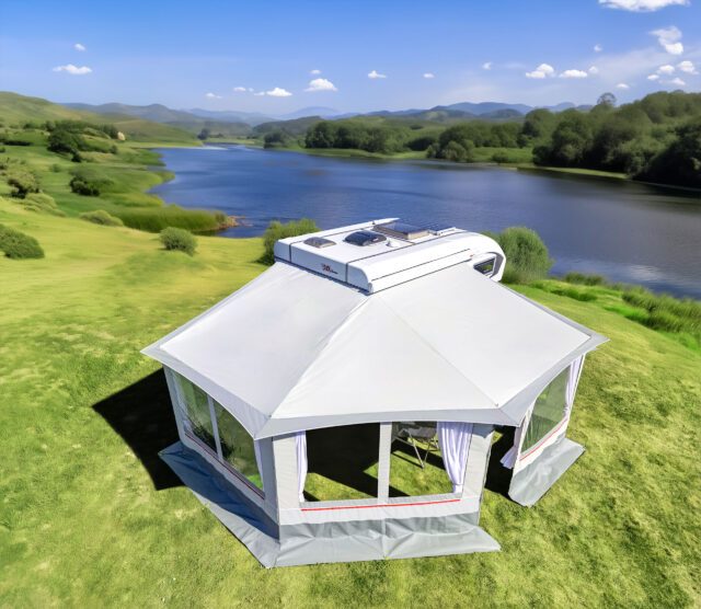 Freistehendes Tischer Vorzelt mit Dachfenster, aufgebaut auf Wiese neben Flusslandschaft.