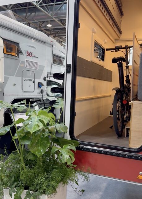 Fahrrad im Innenraum einer Tischer Wohnkabine, Zugang durch geöffnete Tür, Pflanze im Vordergrund.