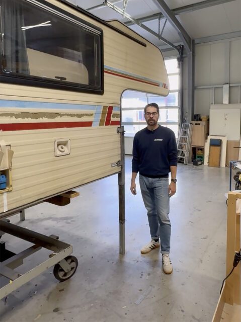 Alte Tischer Wohnkabine im Hallenlager, Person steht daneben – Blick auf Seitenwand und Stützen.
