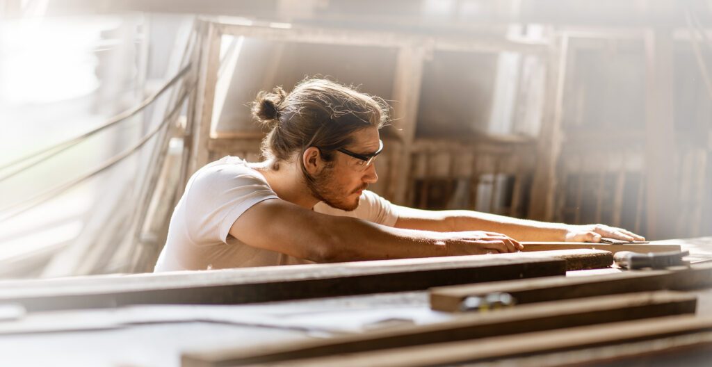 young carpenter man using sandpaper on a piece of wood in workshop .